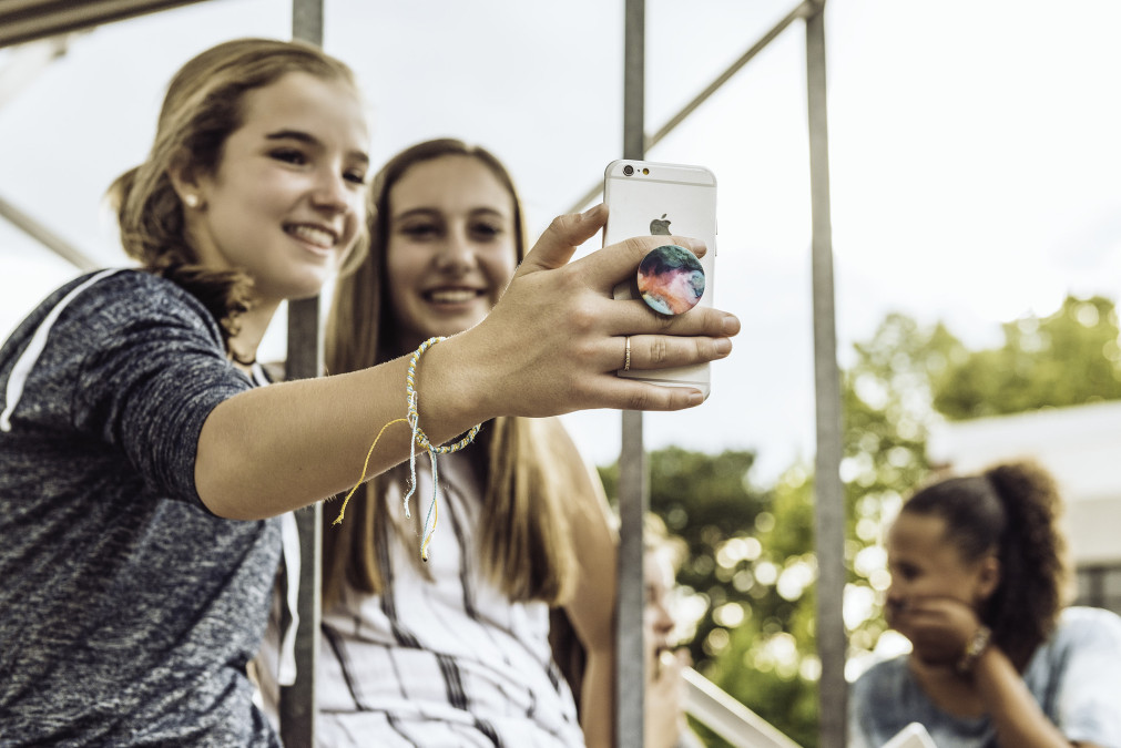 Two teenage girls taking selfie using iPhone equipped with PopSocket